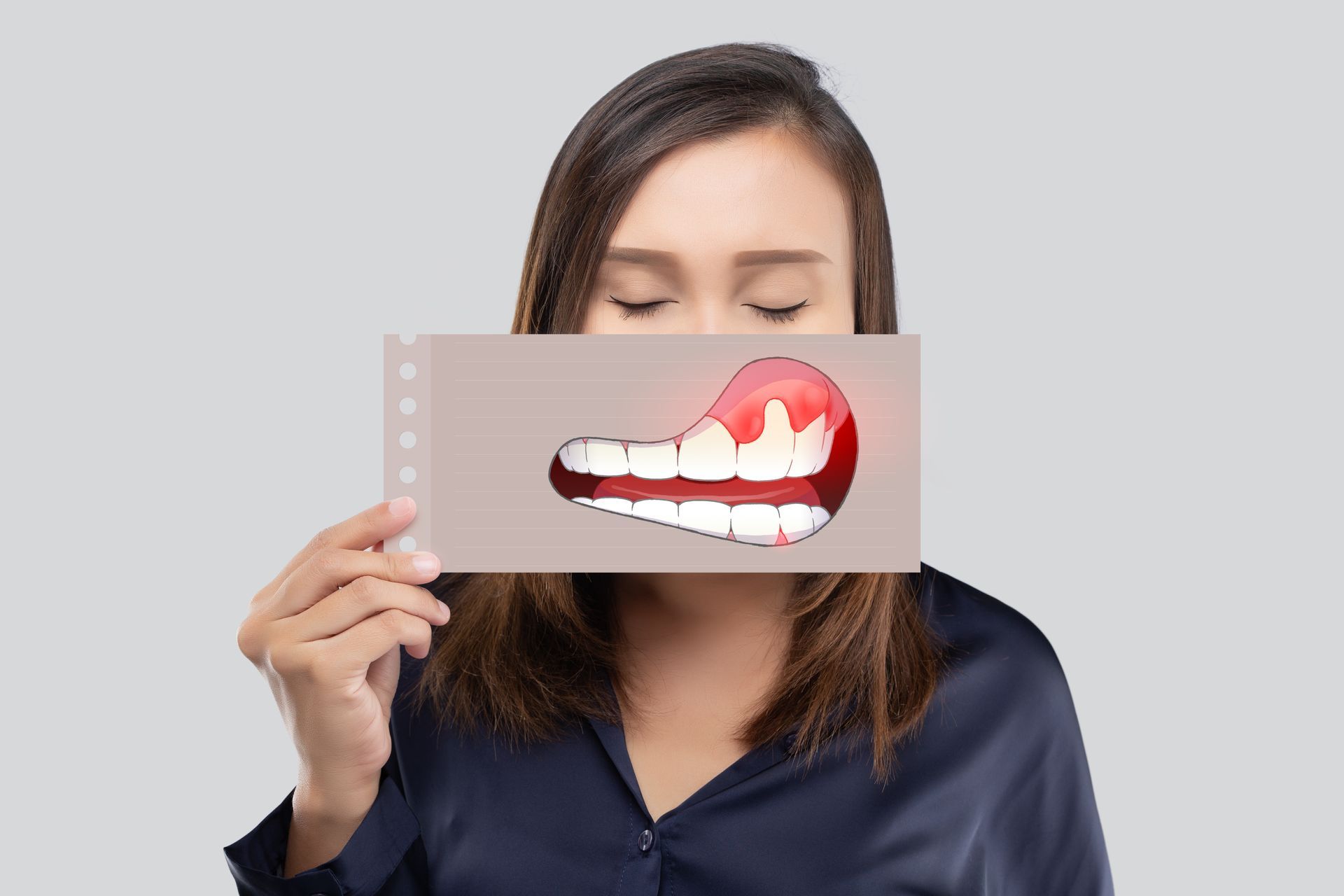 A person holds a card over their mouth depicting red, inflamed gums, representing gum disease symptoms.