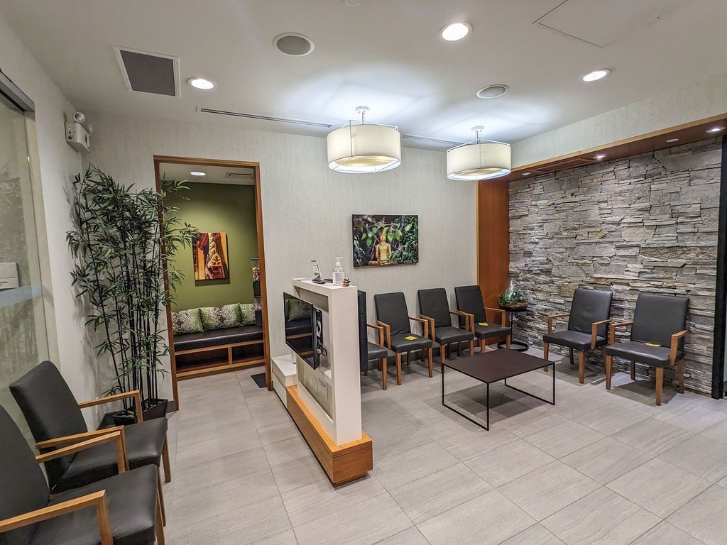 A modern waiting room featuring a stone wall, multiple dark leather chairs, a small coffee table, and hanging lamps.