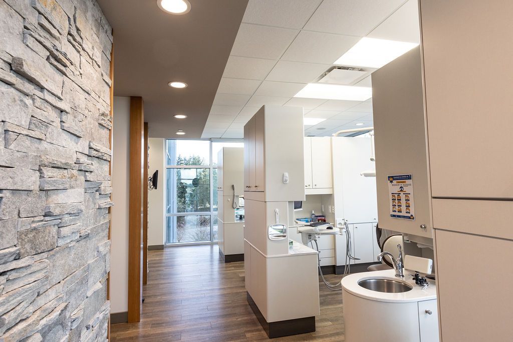 A brightly lit dental office hallway with stone accent walls, wooden flooring, and white cabinetry.