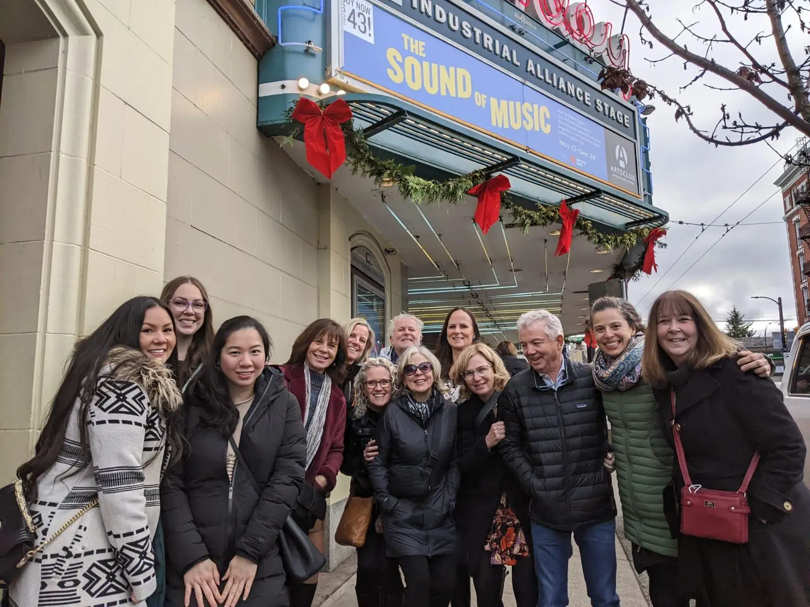 A smiling group stands in front of a historic theater marquee featuring