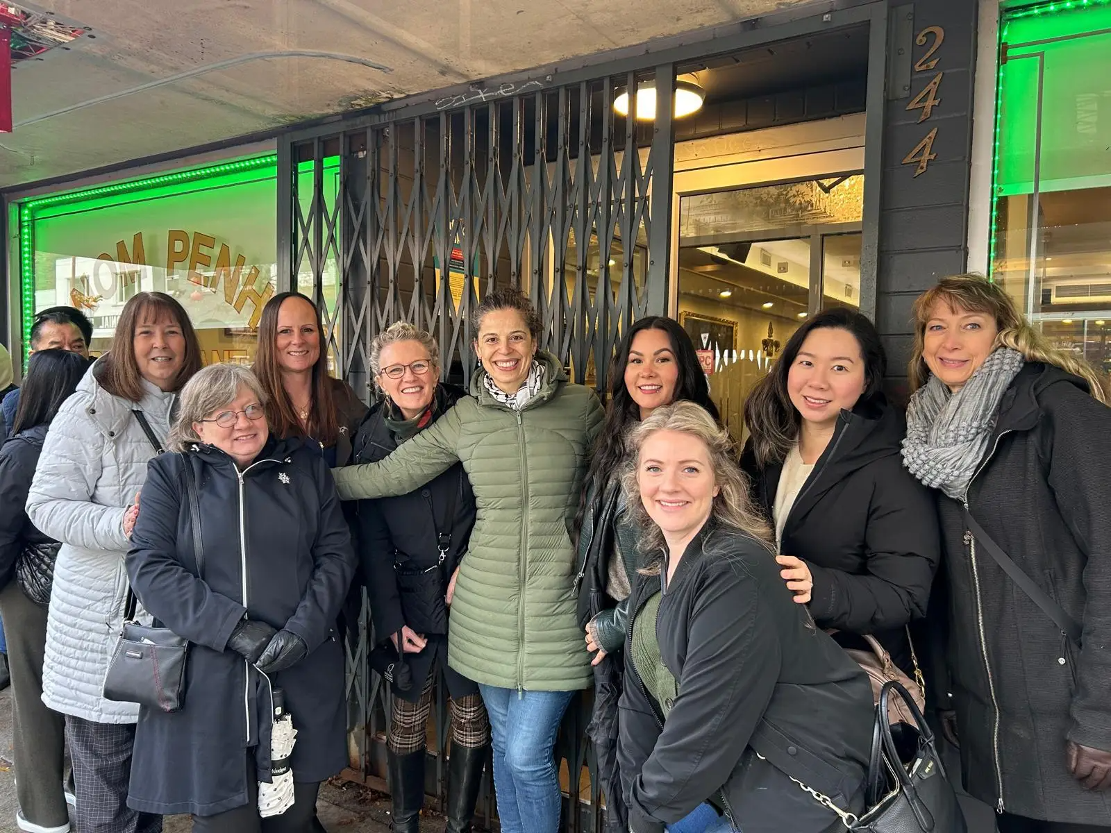 A group of people standing outside a building with a green storefront, smiling and posing for a photo.