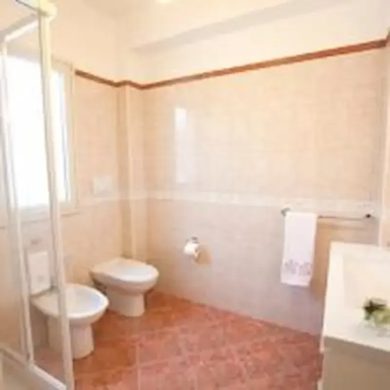 Bright bathroom with bidet, toilet, sink, and bathtub; beige walls and brown tile floor