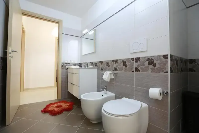 Modern bathroom with white fixtures, gray tile, vanity, and red rug