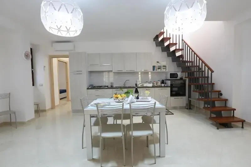Bright minimalist dining area with a staircase, kitchen, and two hanging white pendant lights