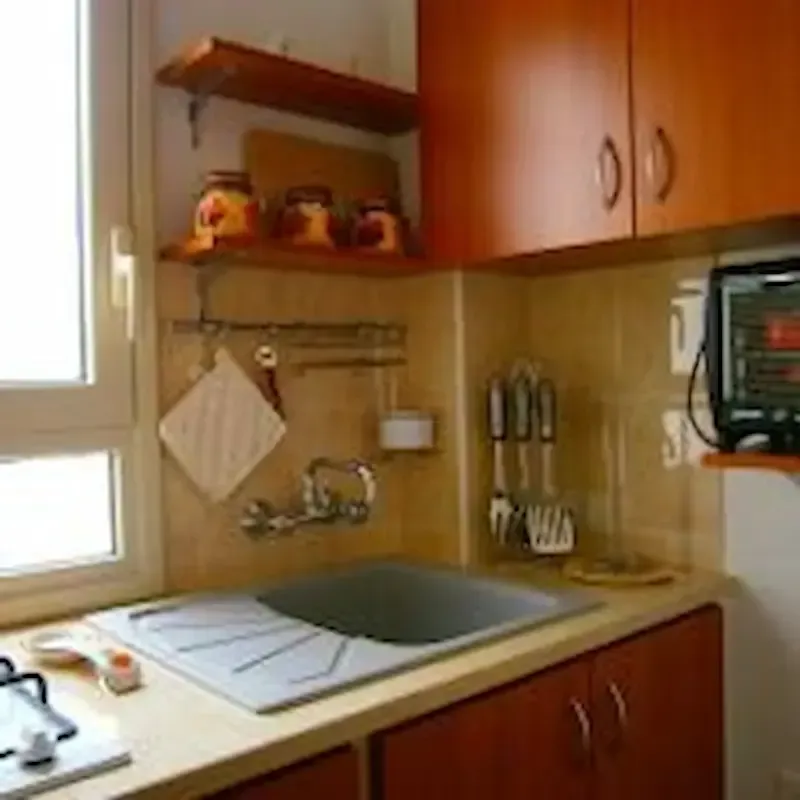 Compact kitchen corner with sink, window, wooden cabinets, and utensils on the wall