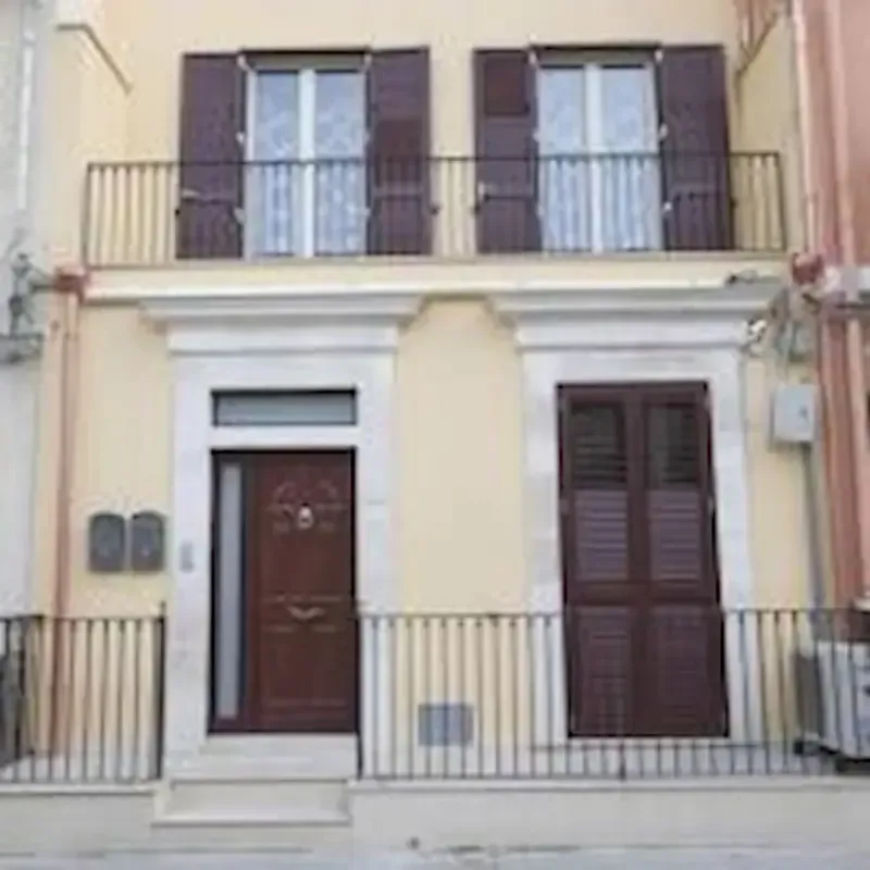 Two-story beige townhouse with brown shutters, central door, and balcony railings