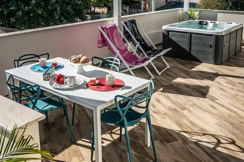 Patio with white table, teal chairs, folded lounge chairs, and a hot tub on a wooden deck