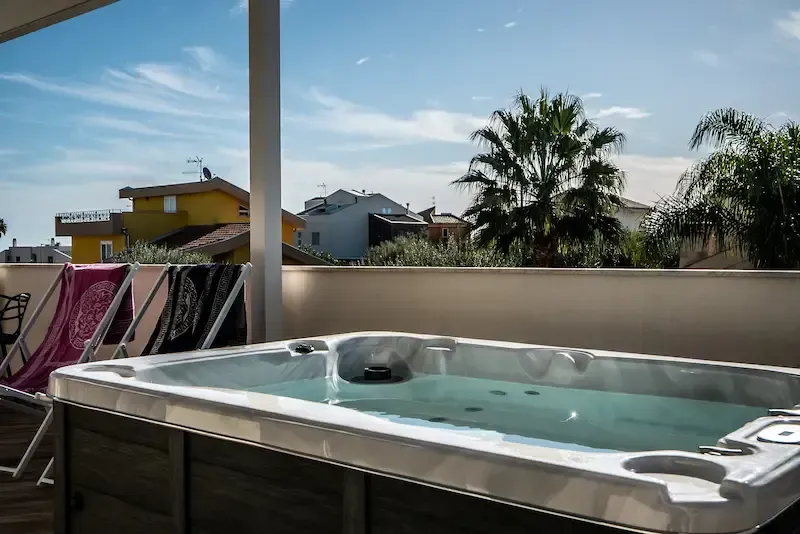Rooftop hot tub with clear water beside lounge chairs under a blue sky, palm trees in the background