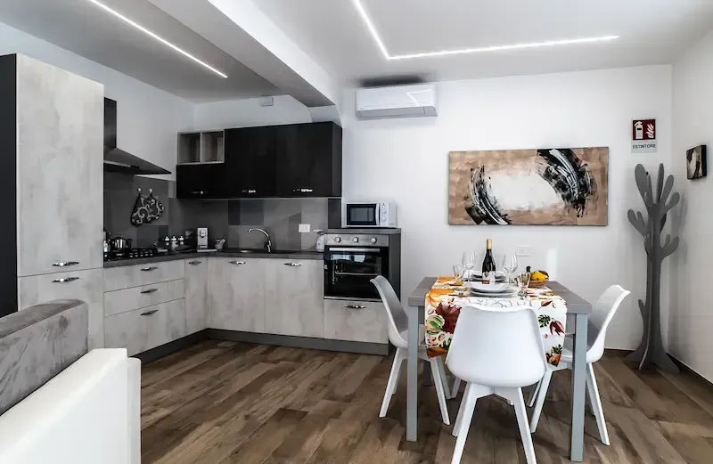 Modern open-plan kitchen and dining area with white cabinets, wood floors, and a set table near a cactus decor piece