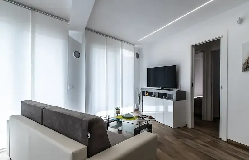 Modern living room with gray sofa, white TV stand, wood floor, and large curtains.