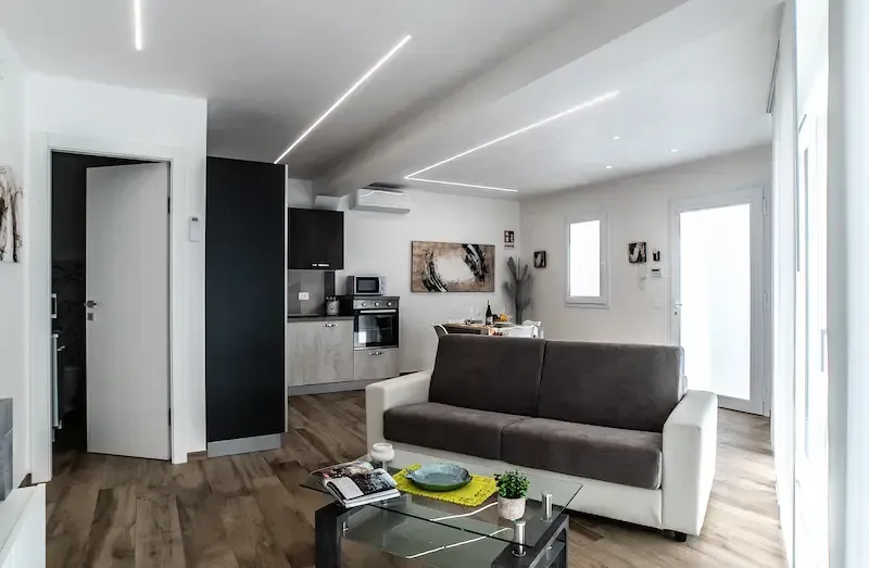 Modern open-plan living room with gray sofa, glass coffee table, and kitchen in the background