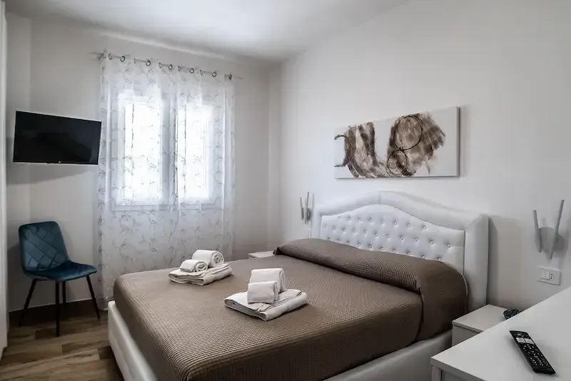 Bright bedroom with a bed, wall art, TV, blue chair, and sheer-curtained window