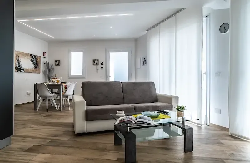 Modern open-concept living room with gray sofa, glass coffee table, and dining area in the background