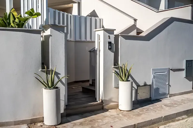 Stella Polares Villa modern white house entrance with potted plants, steps, and a metal gate under bright sunlight