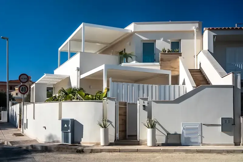 White modern houses with balconies and stairs along a street under a clear blue sky