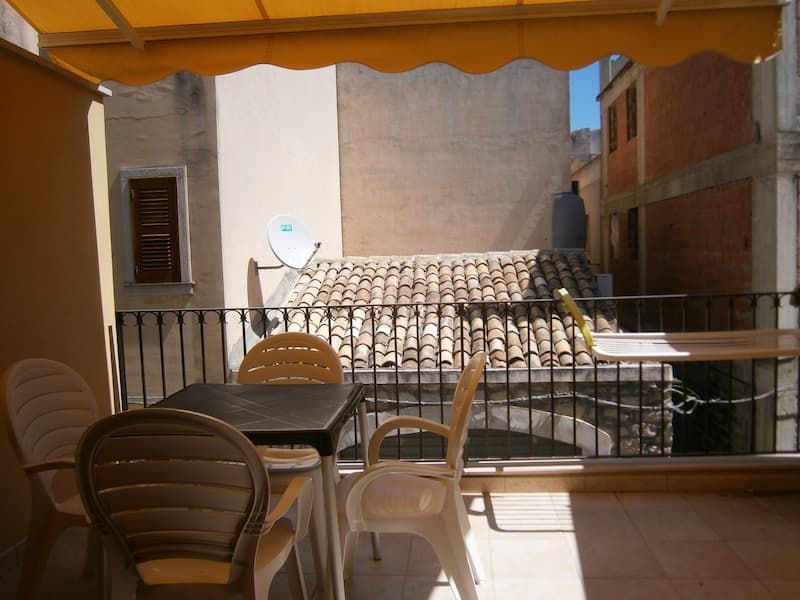 Balcony patio with plastic chairs, table, and orange awning overlooking neighboring rooftops