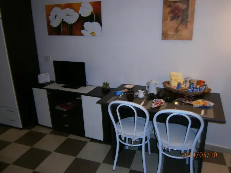 Small dining area with two white chairs, a table of items, desk, and wall art on a checkered floor.