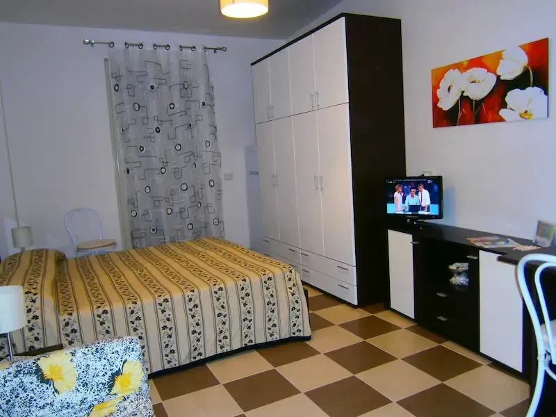Small bedroom with bed, wardrobe, desk, patterned curtains, and checkerboard floor