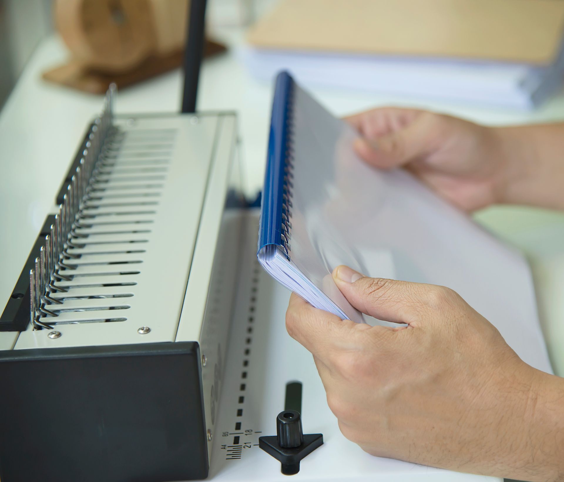Hands flipping through a stack of papers beside a binding machine
