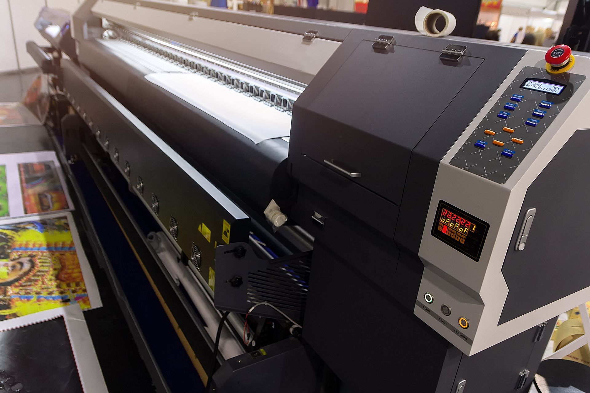 Large-format printer with control panel, printing a colorful graphic sheet in an indoor shop.