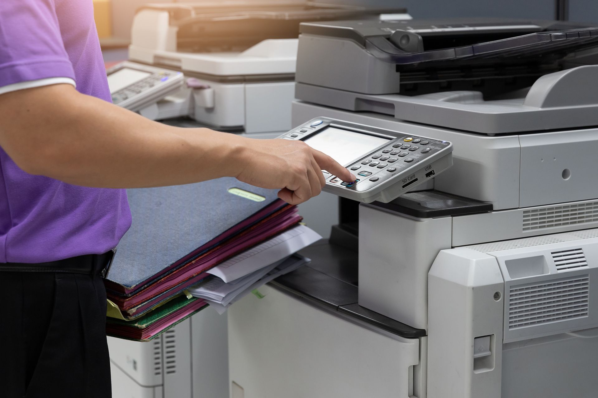 Person using a touchscreen on a photocopier in an office, with printed papers in the tray