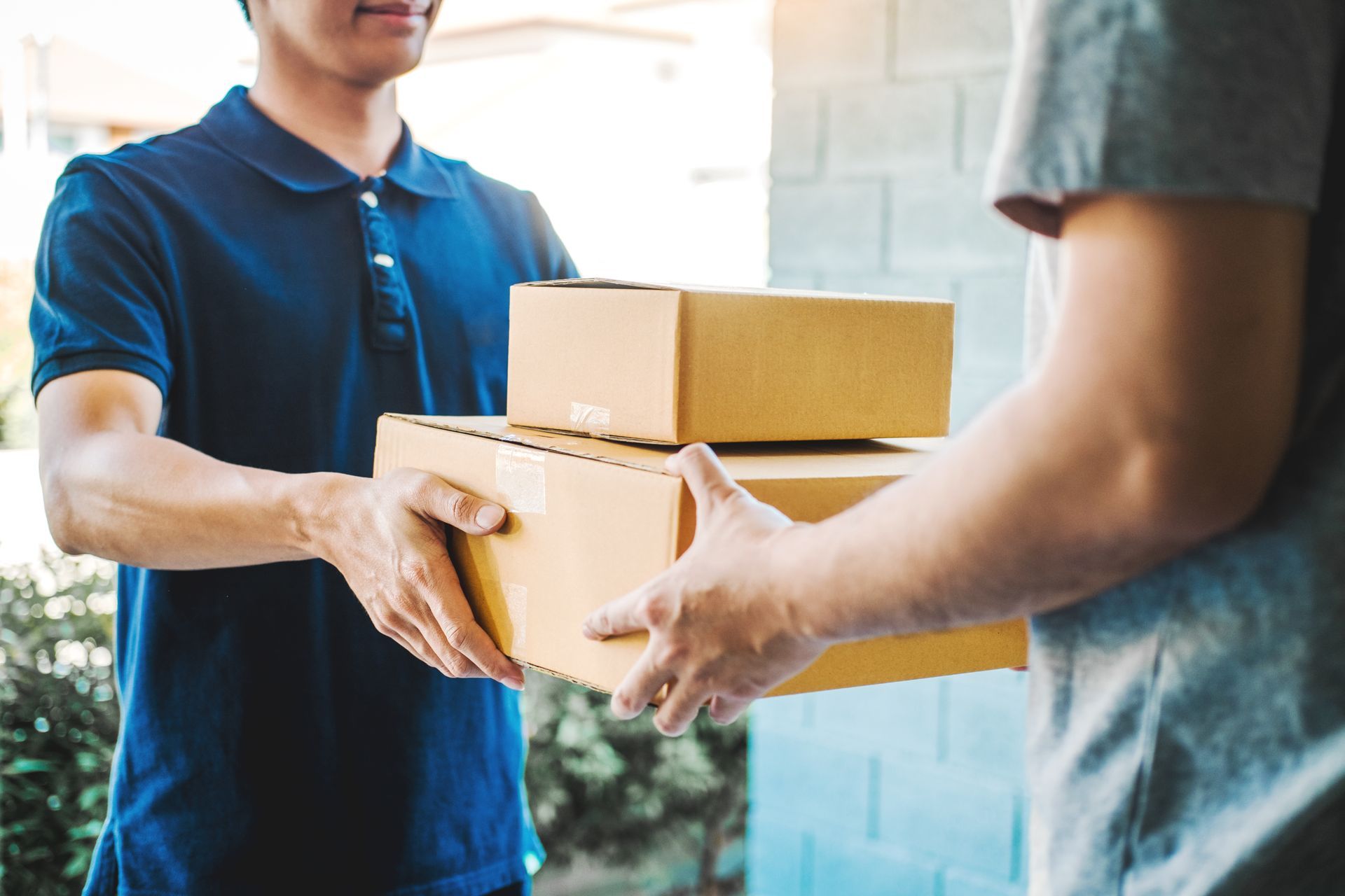 Two people exchanging stacked cardboard boxes at a doorway