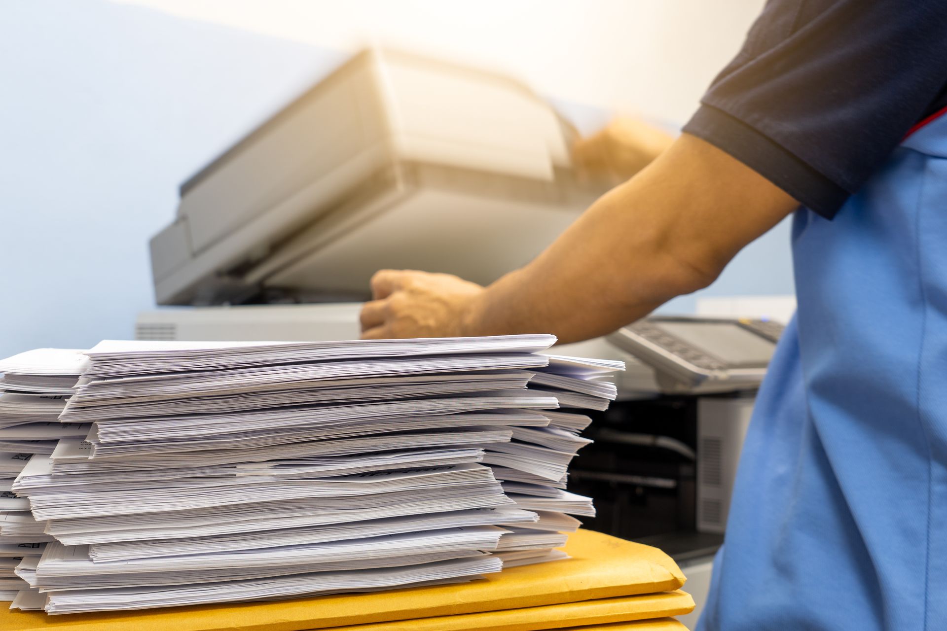 Stack of papers being sorted beside a blue-clad worker in an office or mailroom