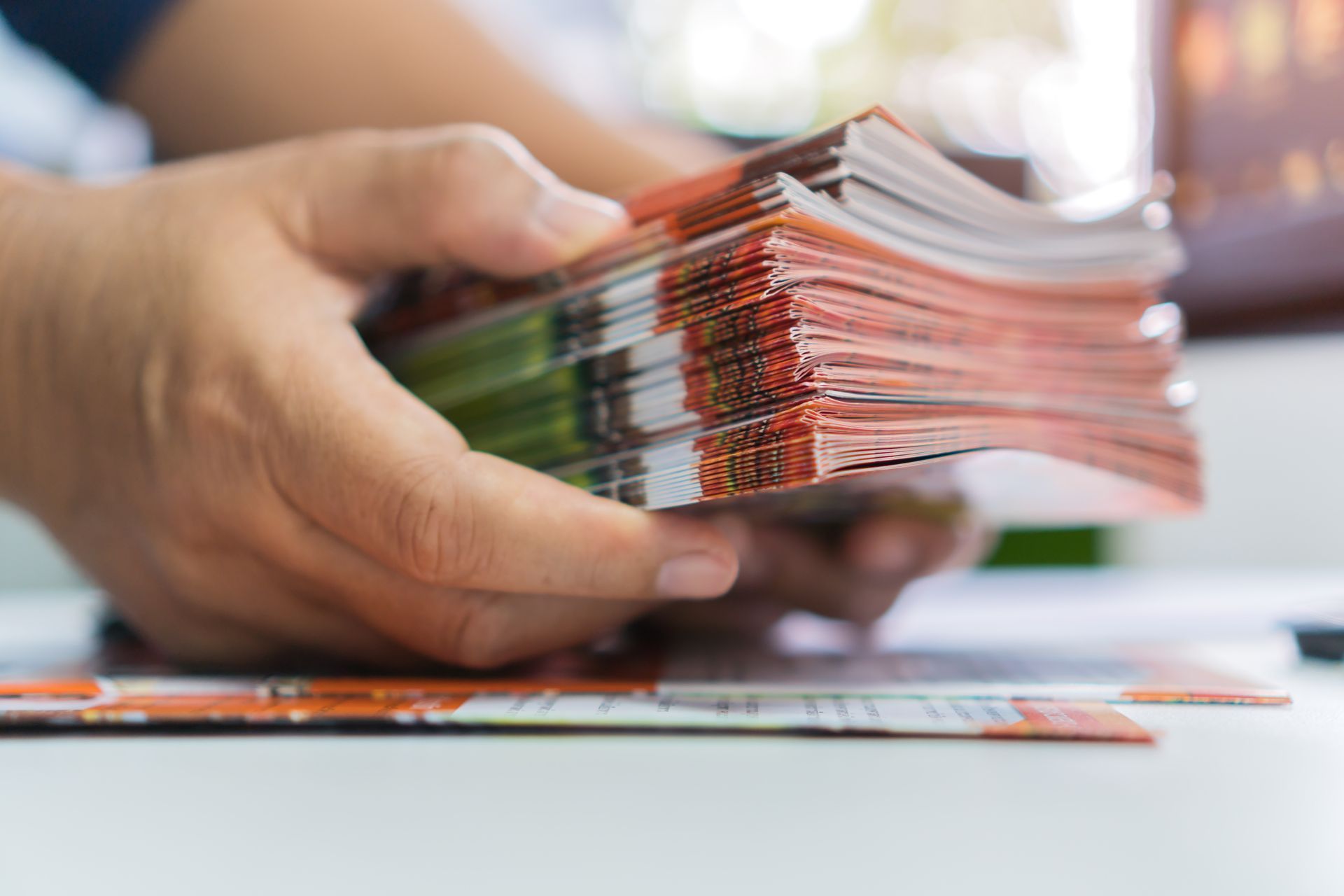 Hands stacking a thick bundle of colorful printed cards on a white table