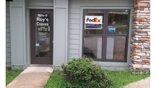 Entrance to Roy’s Coffee with FedEx sign on the glass door, stone wall, and small shrub outside