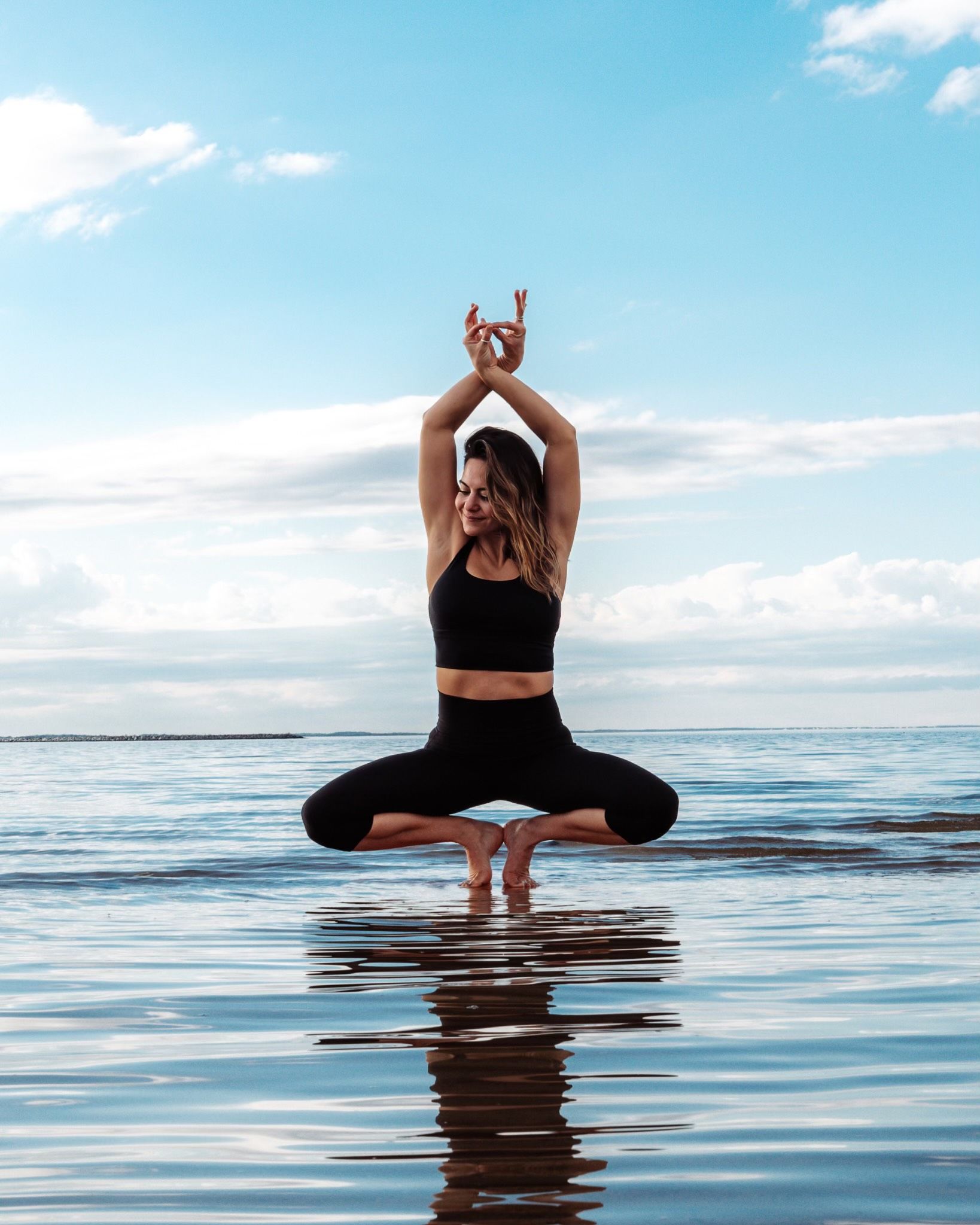 A woman is doing yoga on the beach in the water.