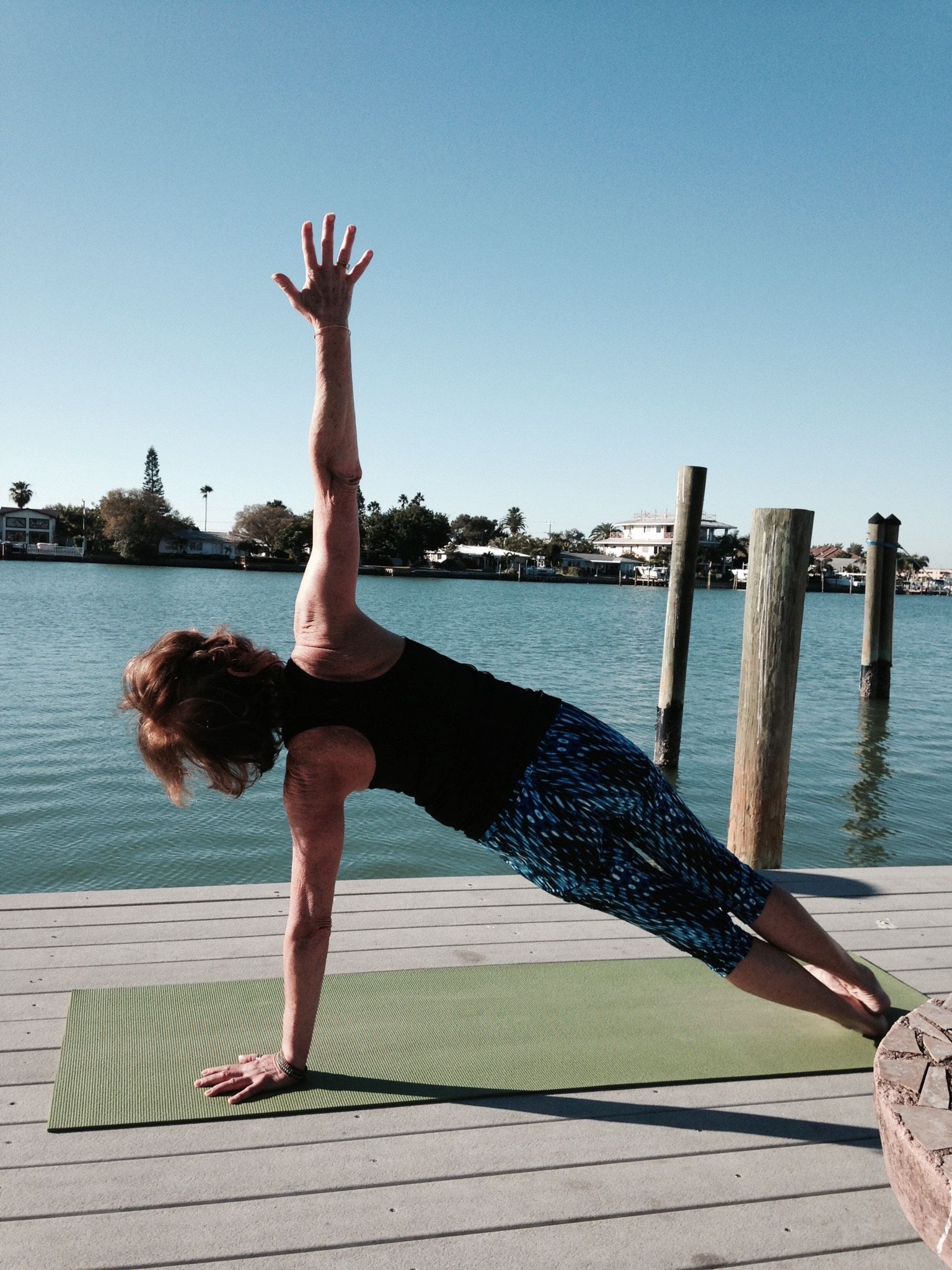 A woman is doing a yoga pose on a dock near the water