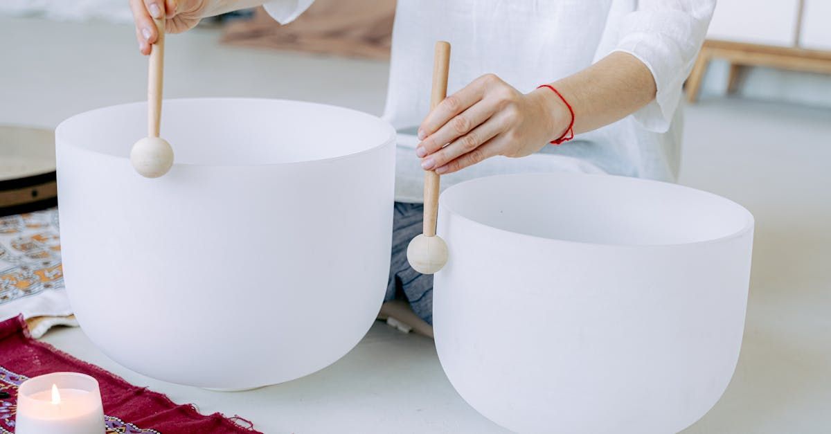 Person playing two white crystal singing bowls with mallets.