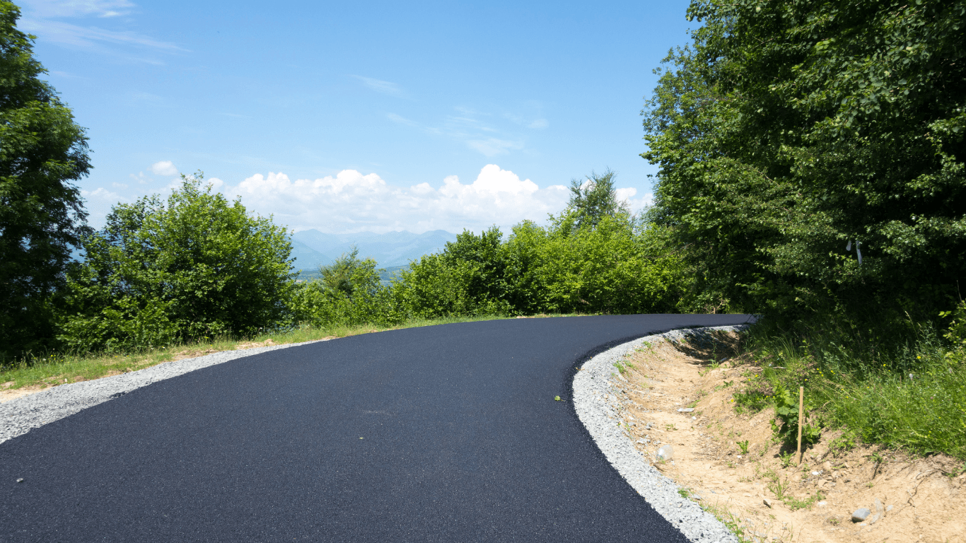 Smooth black asphalt road curving through a green landscape with trees and distant mountains during an asphalt paving service in Centennial, CO