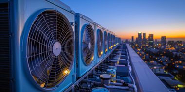 Row of large rooftop cooling fans at sunset with a city skyline in the background