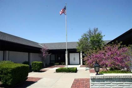 Office building entrance with American flag, walkway, and pink flowering bushes