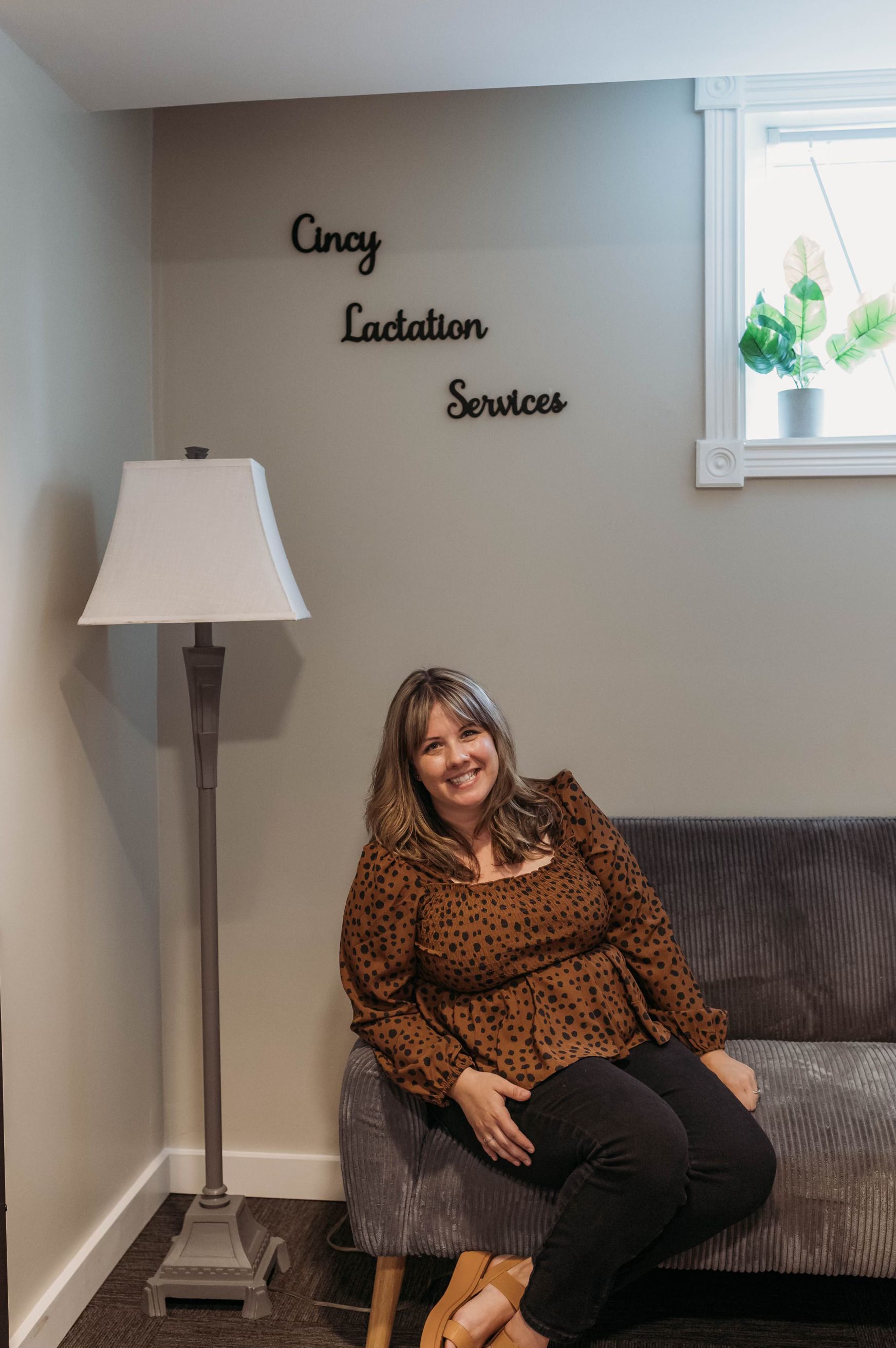 Woman smiles, sitting on a couch.  Sign: 