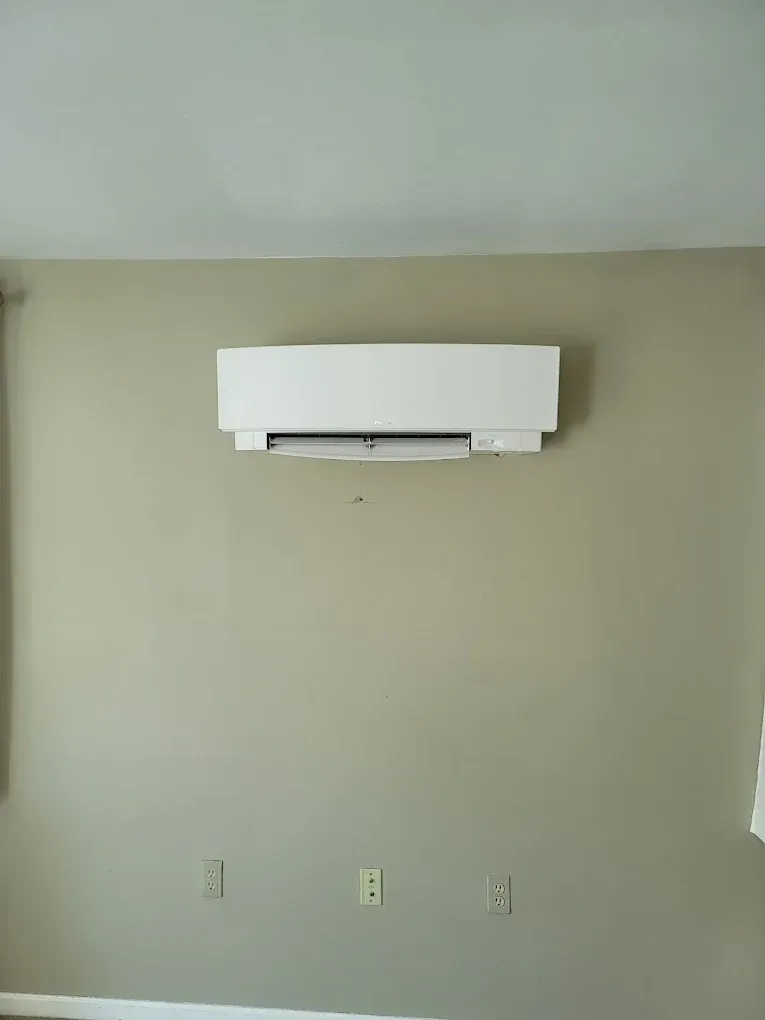 Empty beige room with a white wall-mounted air conditioner near the ceiling.