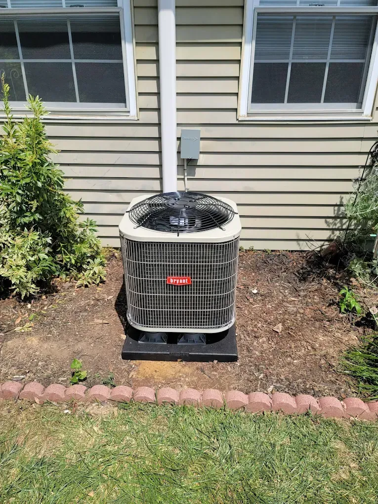 Outdoor HVAC condenser unit beside a house with beige siding and a small garden bed
