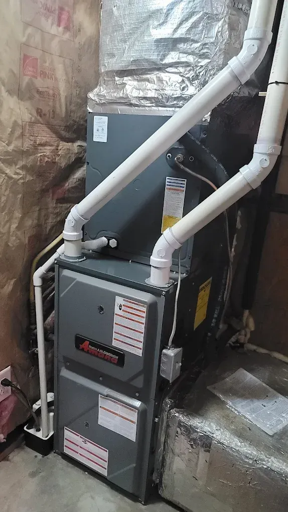 Two gray HVAC/furnace units in a basement with white duct pipes and insulation nearby