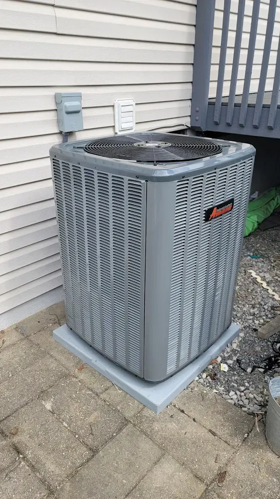 Outdoor gray air conditioner unit beside a house wall and paver patio.
