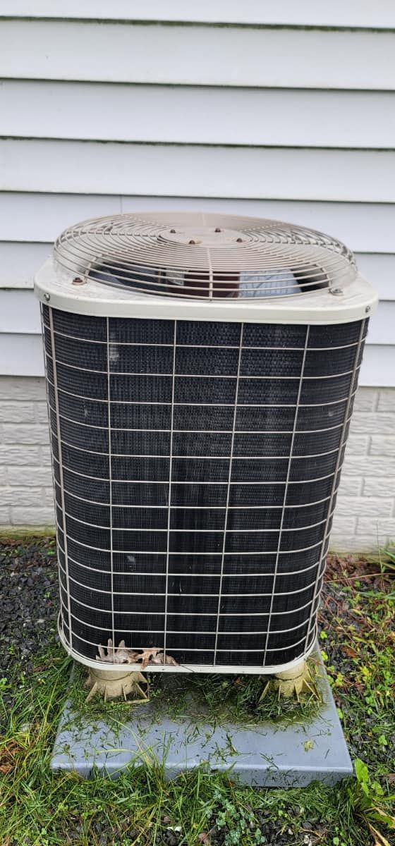 Outdoor air conditioner unit beside a house, with a dirty top fan and rust on the base