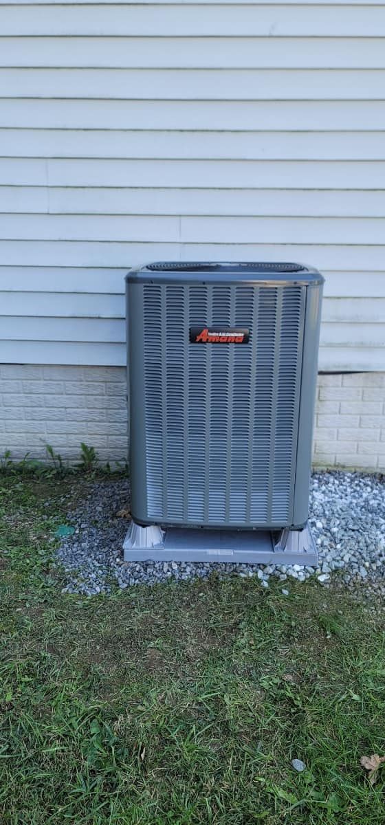 Outdoor air conditioner unit against a white house wall beside grass and gravel