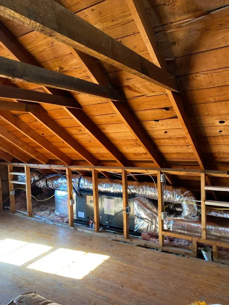 Attic with exposed wooden rafters and insulation, lit by sunlight through a roof opening
