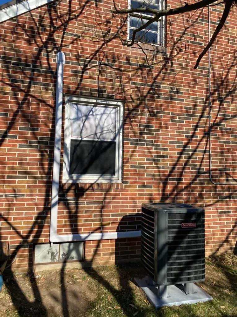 Brick house exterior with window, utility pipe, and air conditioning unit in the yard