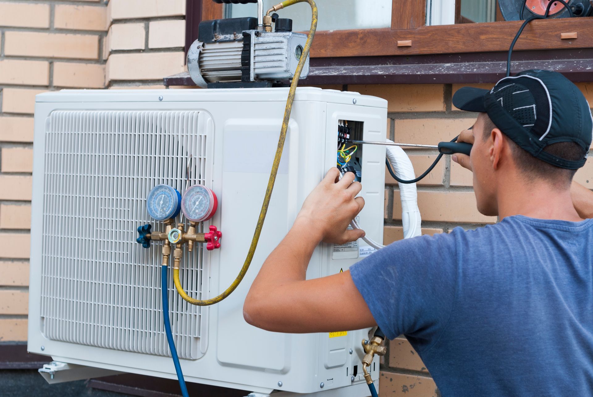 Technician adjusting HVAC unit with gauge hoses mounted on an outdoor brick wall
