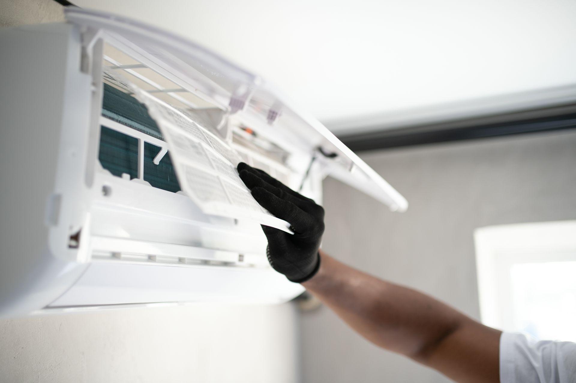 Person cleaning a wall-mounted air conditioner filter with a black glove
