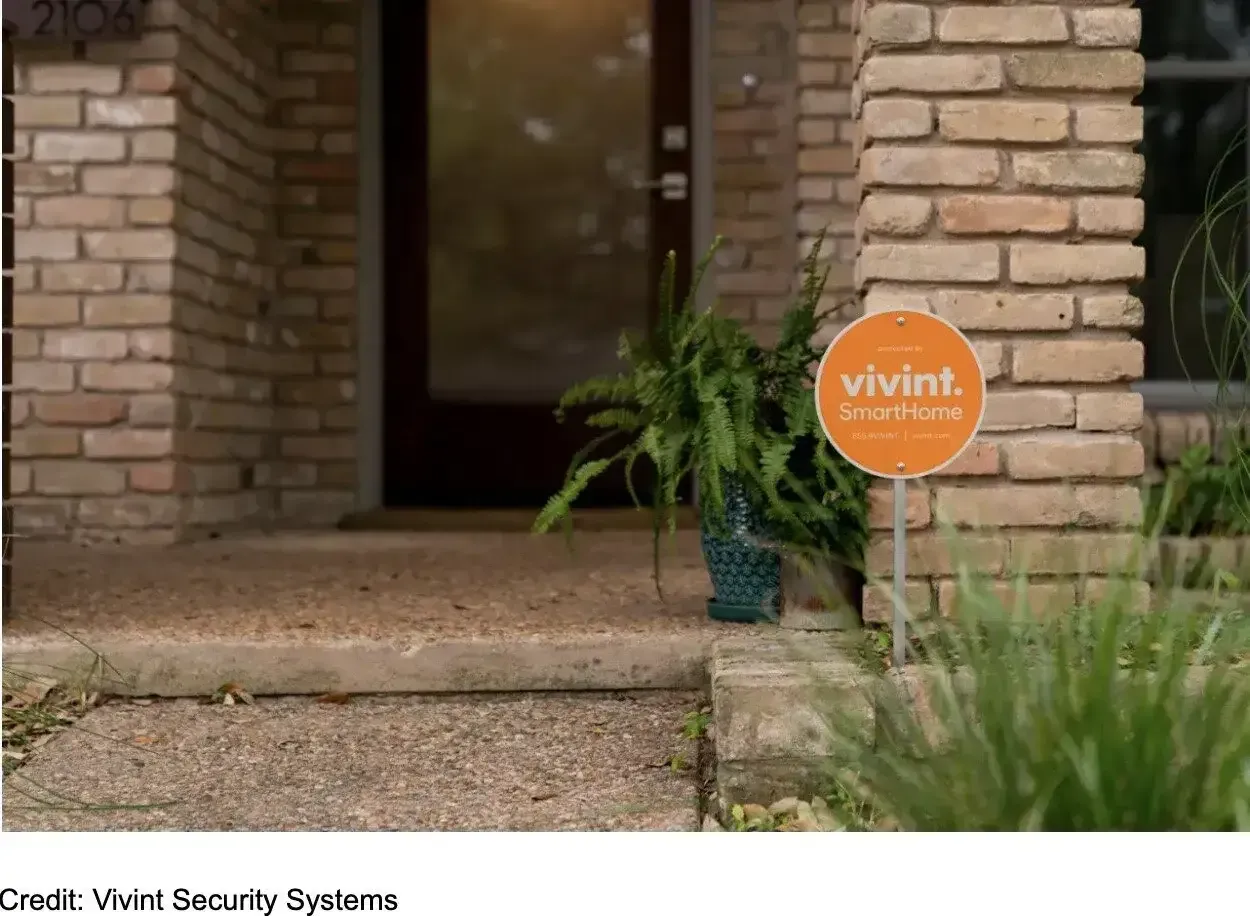 Orange Vivint security sign near a home's front door and brick columns.