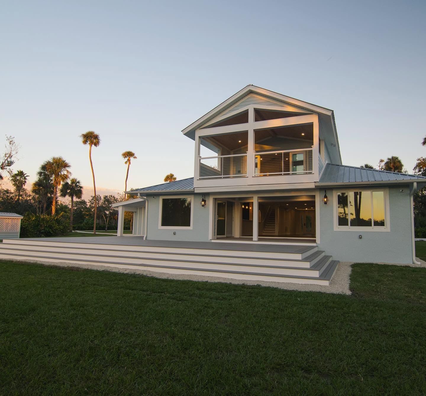Two-story white house with large windows and a grassy lawn at sunset