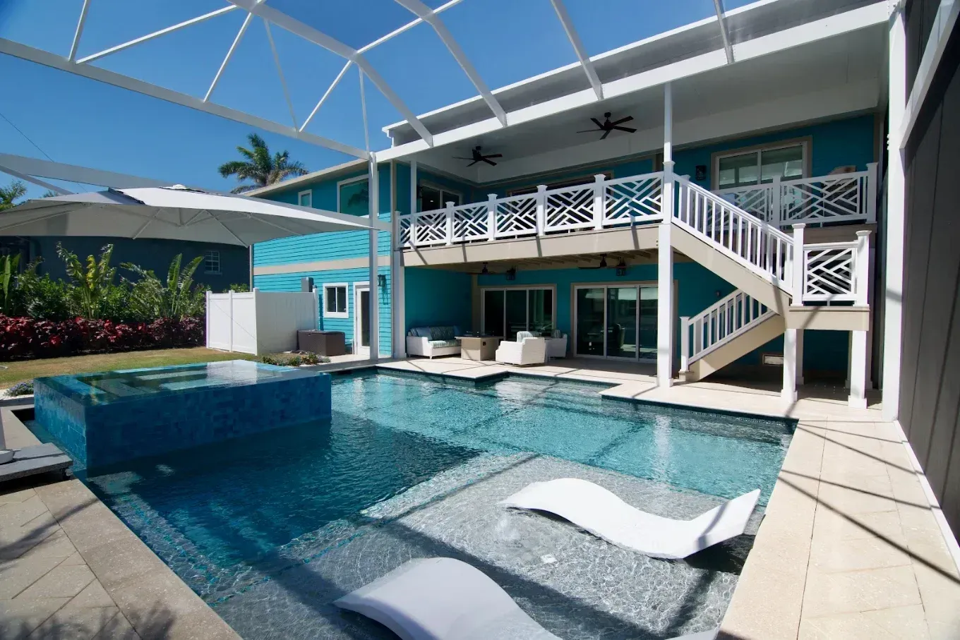 Modern home patio with a turquoise pool, white lounge chairs, and a second-story balcony under a screened enclosure