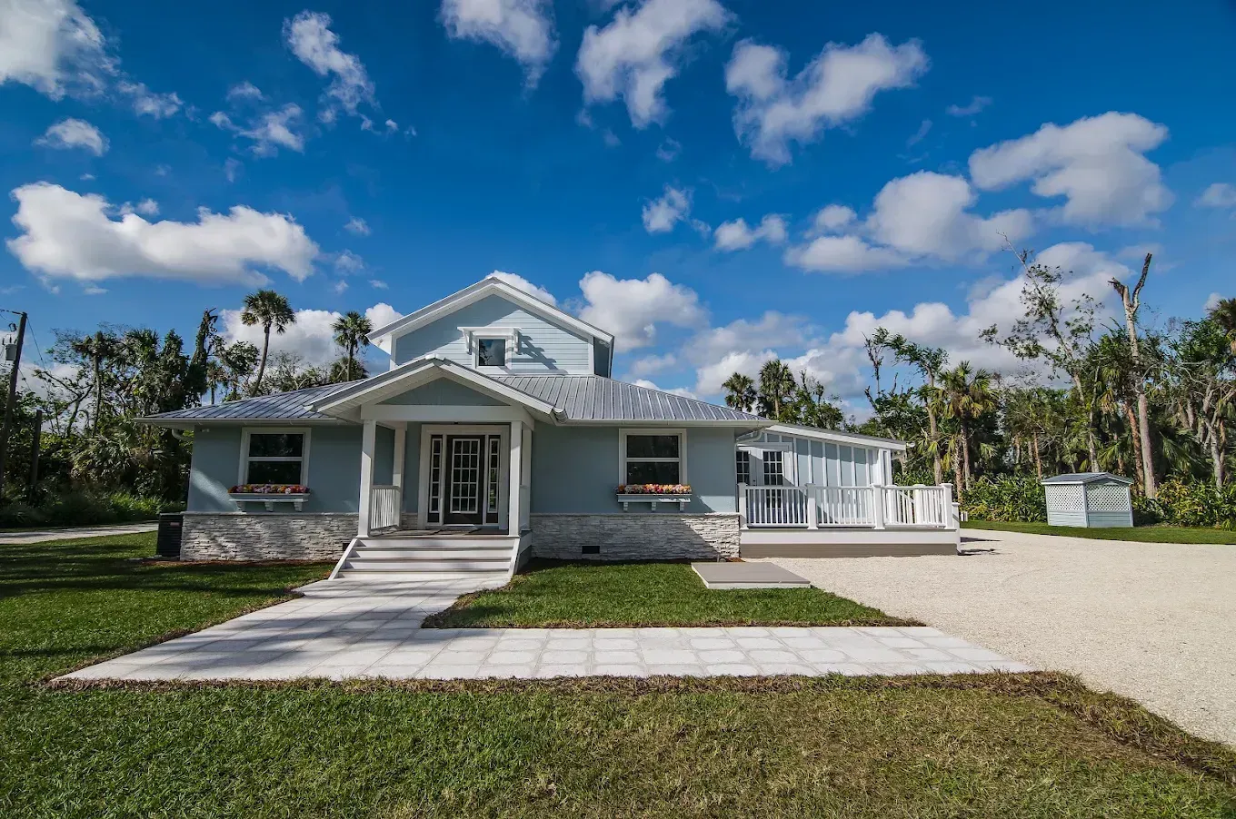 Small white house with a front porch, walkway, and palm trees under a bright blue sky.